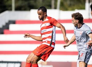 A incrível solidez defensiva do Marco 09 continua a ser o grande destaque da Liga 3. A equipe visitou o São João de Ver, empatou em 0 a 0 e chegou à quinta rodada sem sofrer um único gol na competição. O resultado, o quarto empate sem gols do Marco 09 no campeonato, mantém o time da casa, São João de Ver, ainda sem nenhuma vitória. O JOGO A primeira etapa teve o Marco 09 criando as melhores oportunidades, muitas delas com o atacante brasileiro Kibe. Logo aos 4 minutos, ele serviu um companheiro que desperdiçou uma chance clara na pequena área. O time visitante ainda acertou a trave nos acréscimos, em uma cabeçada de Pedro Ribeiro. O São João de Ver, que contou com o brasileiro Washington atuando na defesa, teve mais aproximações à área adversária, mas sem criar perigo real. Na segunda etapa, o Marco 09 foi mais ofensivo em busca da vitória. A equipe visitante, liderada pelo brasileiro Kibe, chegou a balançar as redes logo no primeiro minuto, mas o gol do atacante foi corretamente anulado por impedimento. Aos 54, Kibe teve outra chance de ouro para marcar com o gol aberto, mas um zagueiro adversário fez um corte providencial para salvar o que seria o primeiro gol do jogo. O técnico do Marco 09 tentou de tudo, promovendo a saída de Kibe e a entrada de outro atacante brasileiro, Marllon, aos 83 minutos. Apesar da pressão visitante, a equipe não conseguiu furar a defesa da casa, que também teve uma chance no fim, mas sem sucesso. A 
